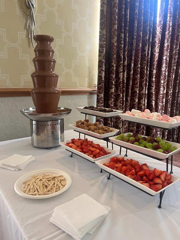 Milk chocolate fountain with tiered platters of brownies, marshmallows, cake cubes, grapes, and strawberries