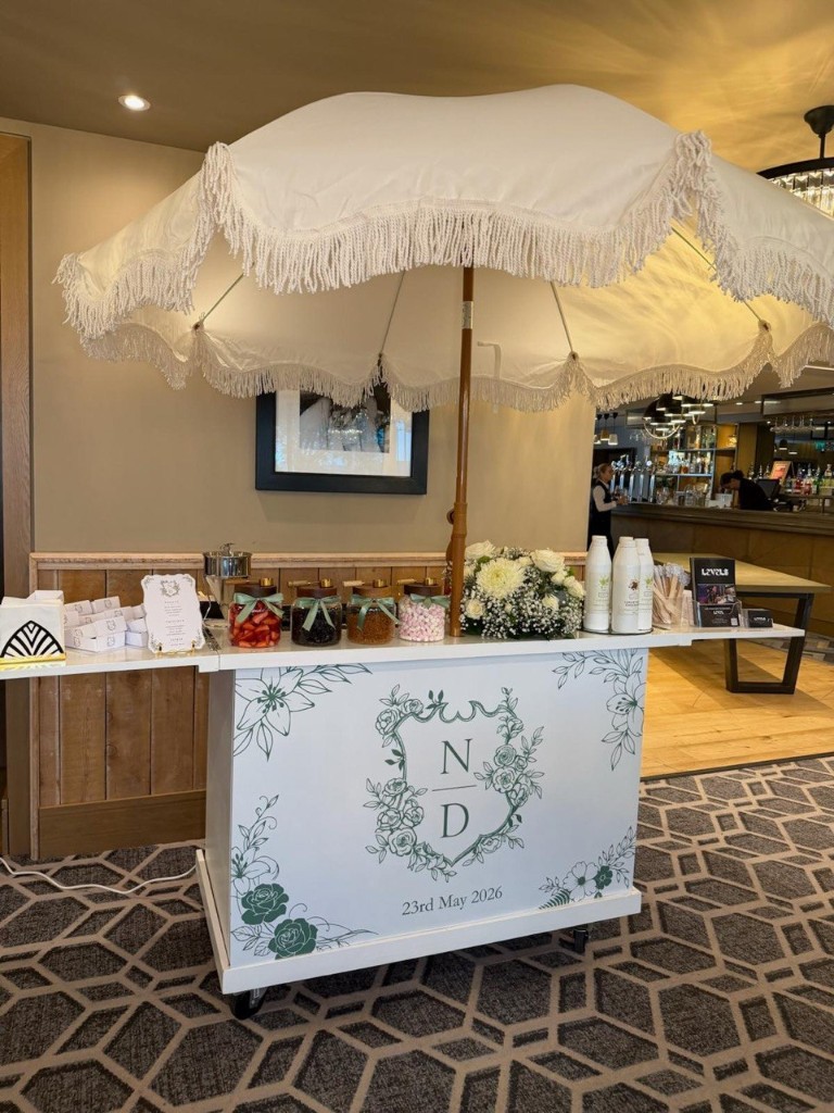 Personalised Levels pancake cart with fringe umbrella, floral branding, and gourmet toppings at a wedding venue