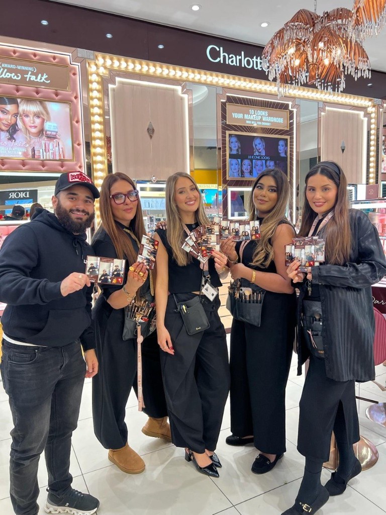 Guests holding printed photo booth strips at a Charlotte Tilbury retail event, with branded makeup displays and vanity lighting